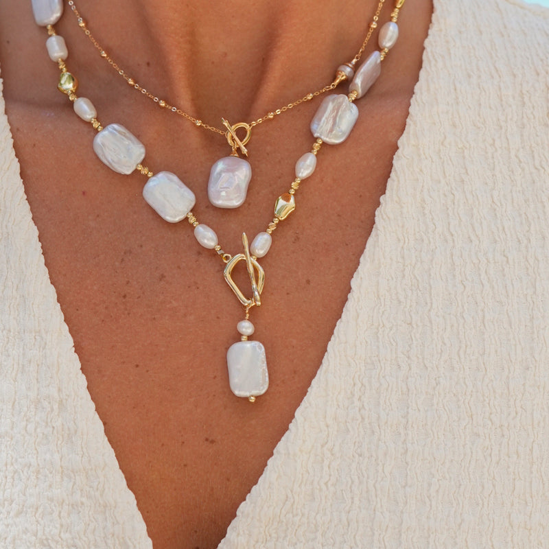 Necklace with white stones and gold clasps on a person wearing a cream top.